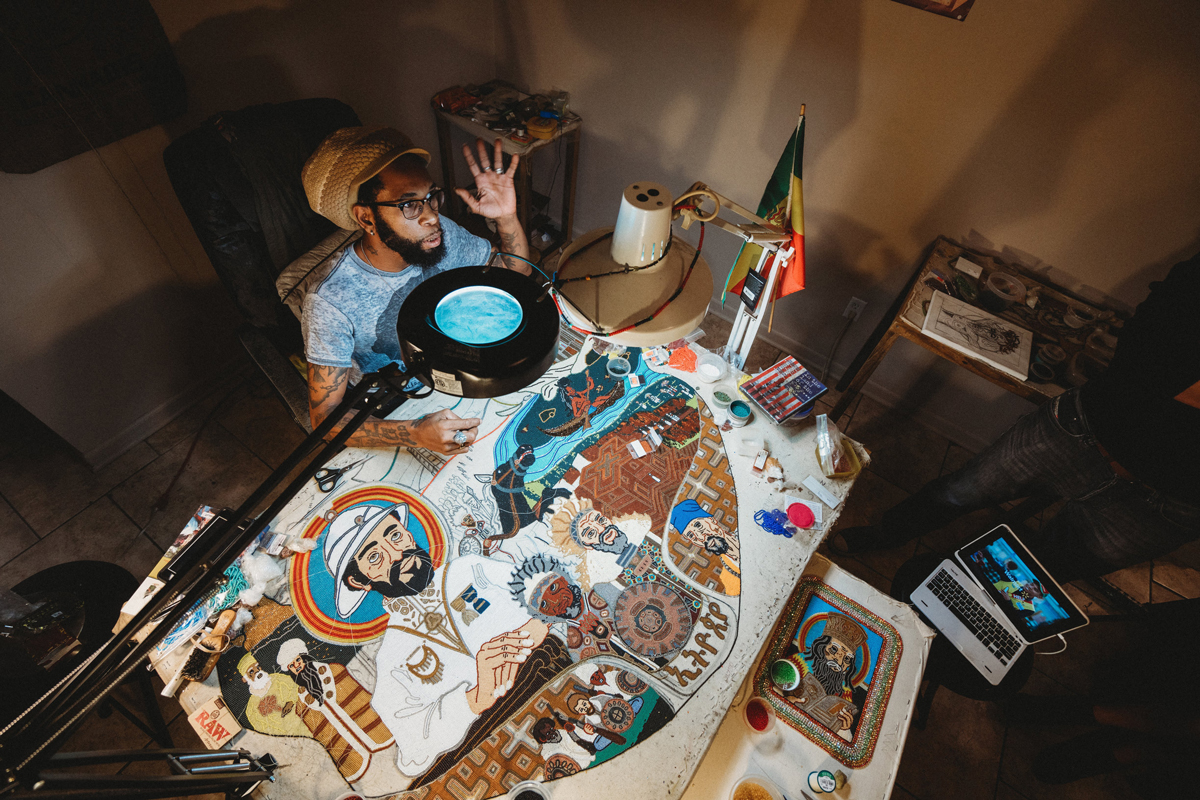 Demond Melancon photographed from above, showing a large lamp illuminating his beadwork on a Madri Gras suit.