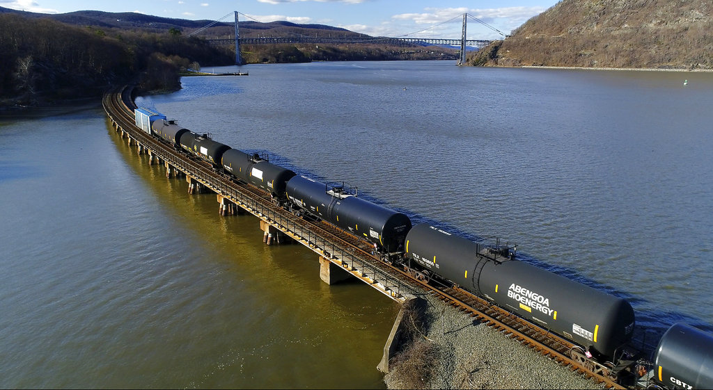 A train of tank cars is pulled by across a mighty but tranquil river.