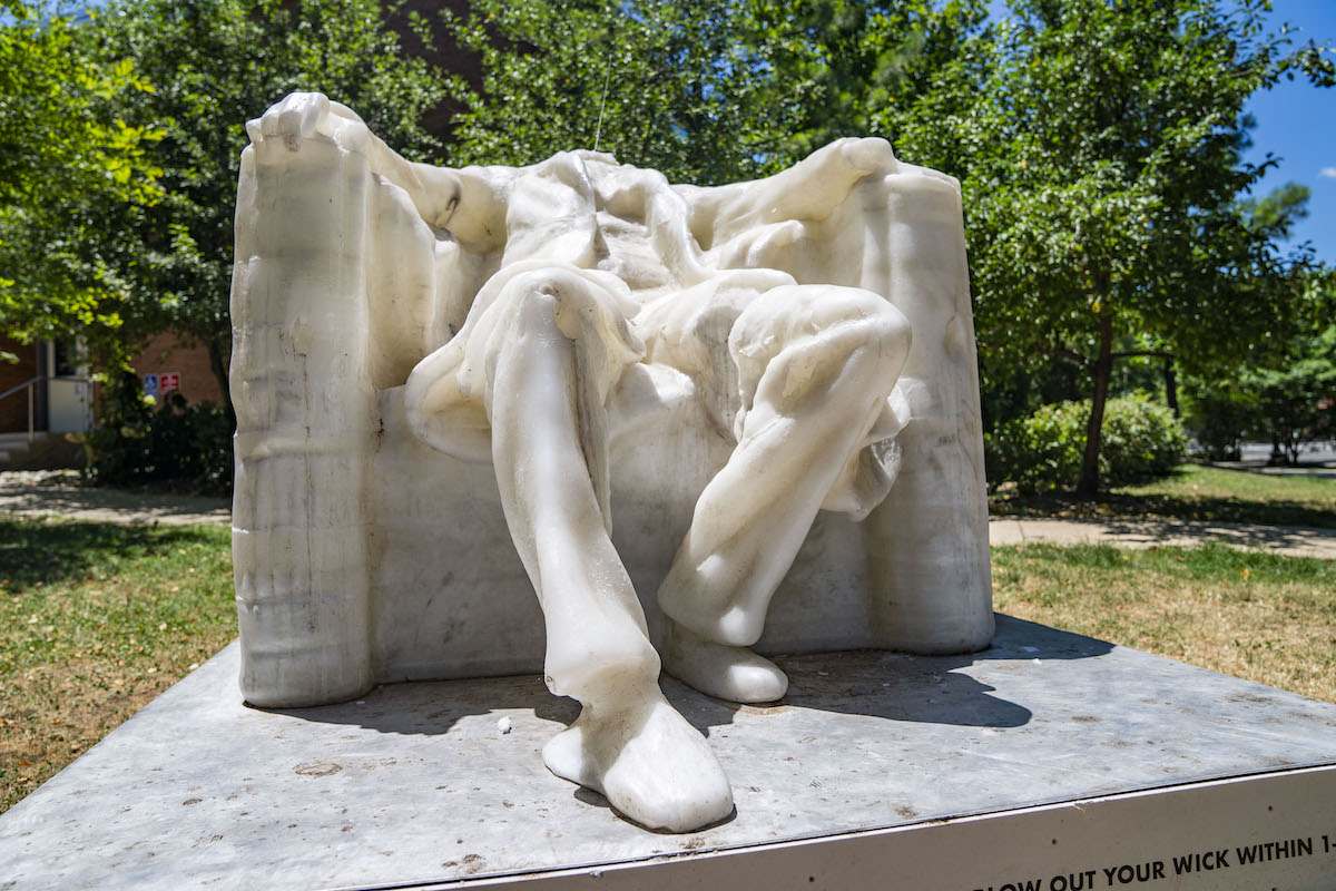 A wax sculpture of a seated person in a chair with their arms resting on its sides. The head has melted away.