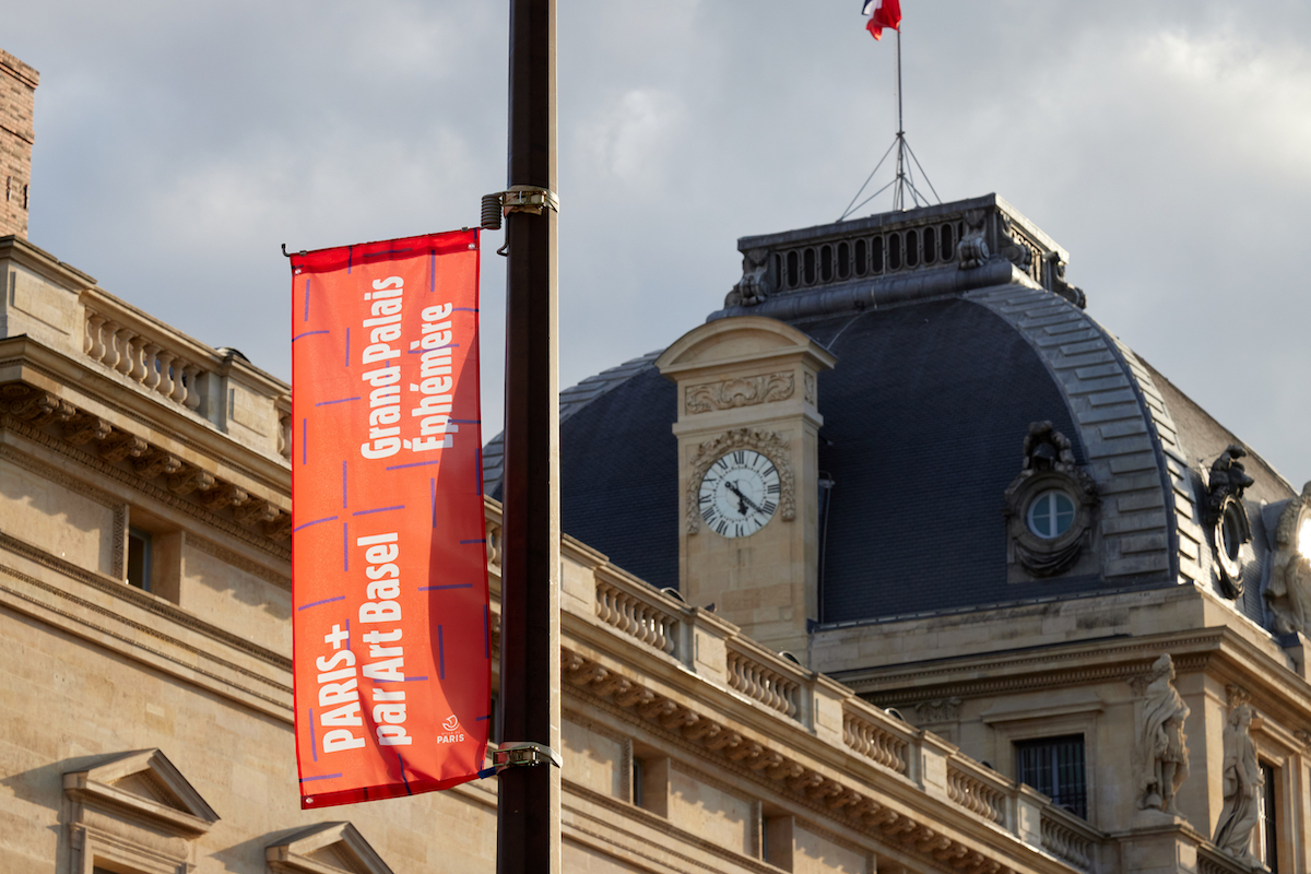 A banner near a rooftop of a 19th-century building in Paris. It advertised 'Paris+ part Art Basel Grand Palais Éphémère'.