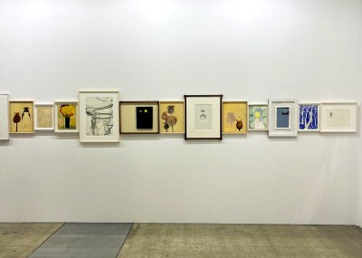 Several small works on paper hang flush against each other in an art fair booth.